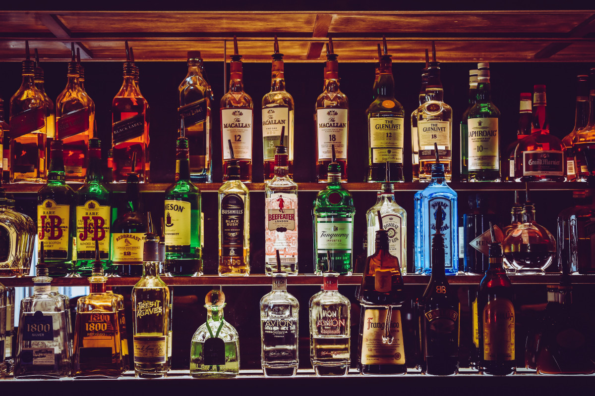 Uma parede de bar com três andares com diversas garrafas de bebidas álcoolicas em pé