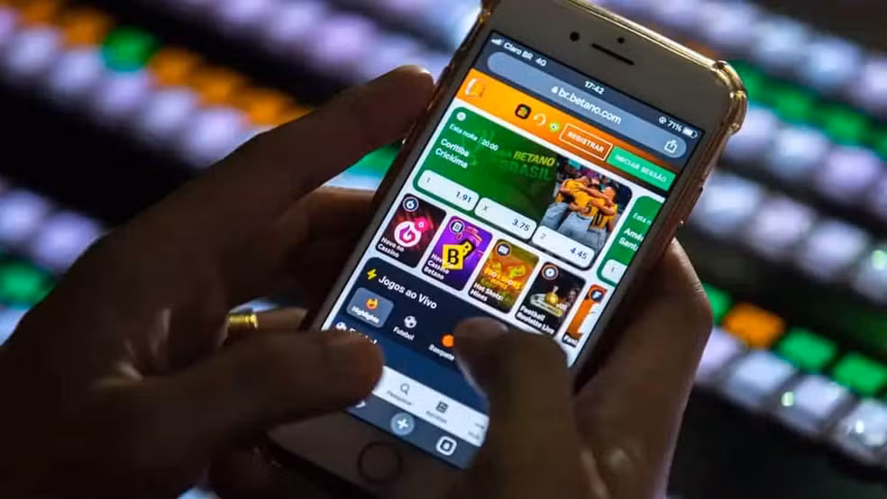 A imagem mostra uma pessoa utilizando um smartphone para acessar uma plataforma digital de apostas, com diferentes opções de jogos exibidas na tela.